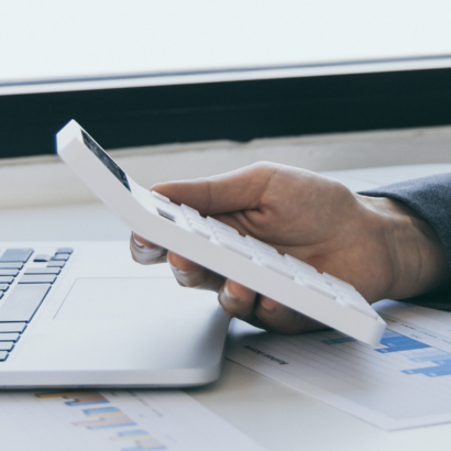 Бизнесмен в костюм държи калкулатор до лаптоп и финансови графики на бюро.