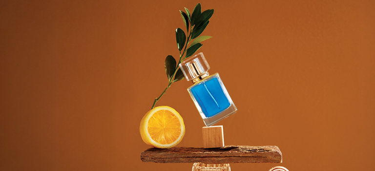 Бутилка със синя течност, половин лимон и клонка с листа върху дърво на оранжев фон.