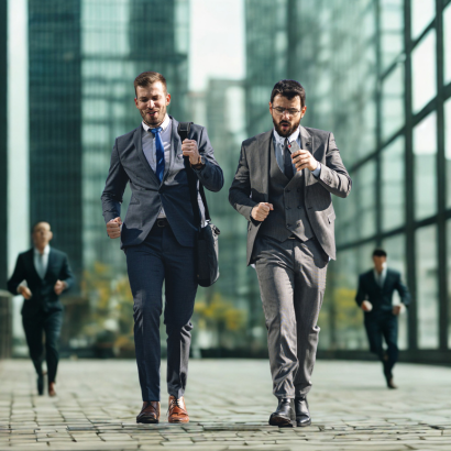 Двама мъже в костюми ходят бързо сред бизнес сгради.